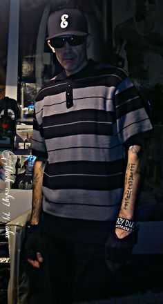 a man with tattoos standing in front of a mirror wearing a baseball cap and striped shirt