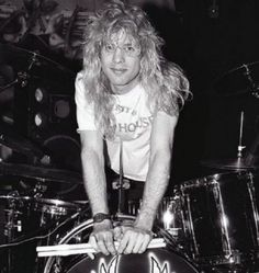 a man with long hair sitting on top of a drum kit in front of drums