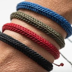 four different colored braided bracelets on someone's arm