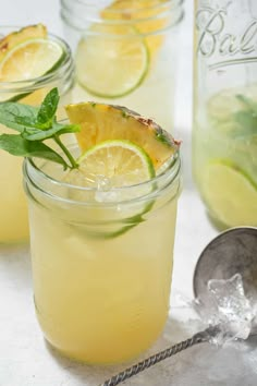 two glasses filled with lemonade and limes next to a jar full of lemonade