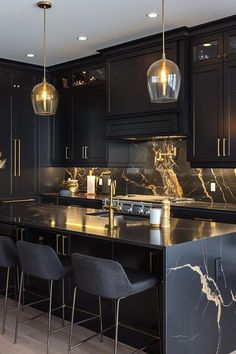 a kitchen with black cabinets and marble counter tops, gold pendant lights over the island