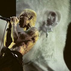 a man with tattoos on his arm holding a microphone in front of a large screen