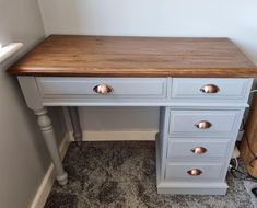 a white desk with two drawers and a wooden top on carpeted floor next to wall