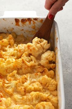 a person holding a wooden spoon in a casserole dish with cauliflower