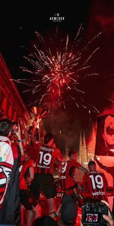 a group of people standing in front of a firework display with red and white shirts on