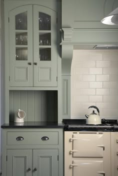 a tea kettle is sitting on the counter in this green and white kitchen cabinetry