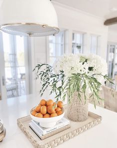 a bowl of oranges sitting on top of a table next to a vase with white flowers