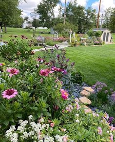 a garden filled with lots of flowers next to a lush green park covered in trees