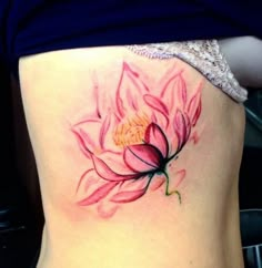 a woman's back with a pink flower tattoo on her left side ribcage