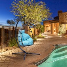 a blue swing chair sitting next to a swimming pool in front of a house at night