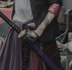 a person with tattoos on their arm holding two swords and wearing gloves, while standing in front of a pile of junk