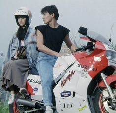 a man and woman sitting on top of a red and white motorbike in the grass