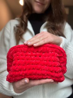 a woman is holding a red crochet purse