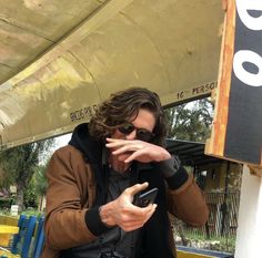 a man holding a cell phone in his right hand and looking at the camera while standing under an umbrella