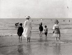 an old black and white photo of people walking in the water at the edge of the beach