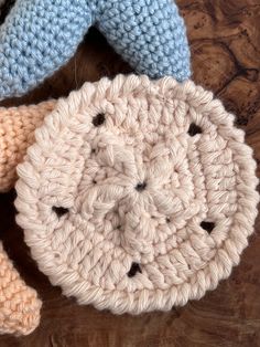 two crocheted items are laying on a wooden surface, one is blue and the other is pink