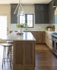 a large kitchen with wooden floors and gray cabinets, an island countertop and two stools