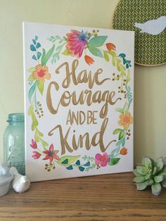 there is a sign that says have courage and be kind on the shelf next to some flowers