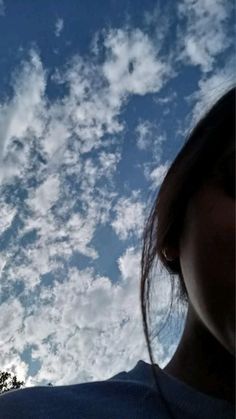 a woman is looking up at the sky with clouds in the back ground and trees behind her