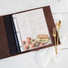 an open menu sitting on top of a table next to a fork and knife