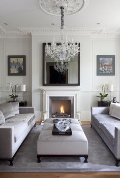 a living room filled with furniture and a chandelier hanging from the ceiling over a fire place