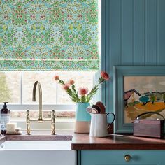 a kitchen with blue cabinets and green roman shades on the window sill above the sink