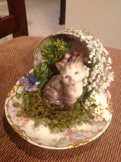 a cat figurine sitting on top of a plate covered in moss and flowers