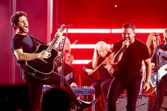 a group of people singing and playing instruments on stage with one man holding a guitar