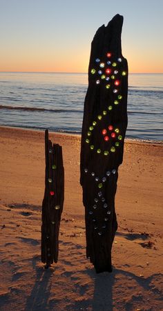 two pieces of driftwood are on the beach at sunset with colorful lights in them