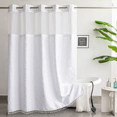 a white shower curtain in a bathroom with a plant on the floor next to it