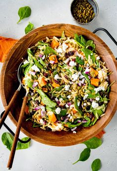 a salad in a wooden bowl with two spoons next to it on a table