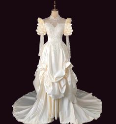 a white wedding dress with long sleeves and ruffles on the skirt is sitting on a mannequin