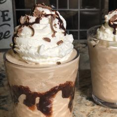 two cups filled with whipped cream and chocolate toppings on top of a marble counter