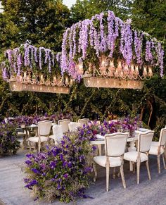 an outdoor dining area with purple flowers and chandeliers hanging from the ceiling above it