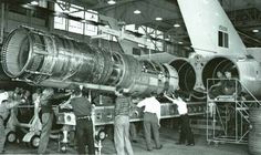 men working on an airplane engine in a factory with other people looking at the machine