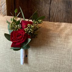 a boutonniere with red roses and greenery on a beige couch cushion