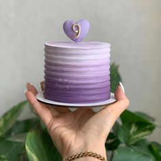 a hand holding a purple cake with a heart on top