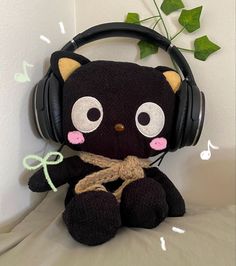 a black cat stuffed animal with headphones on it's ears sitting on a bed