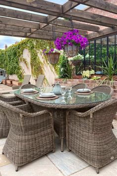 an outdoor dining area with wicker furniture and purple flowers hanging from the ceiling above