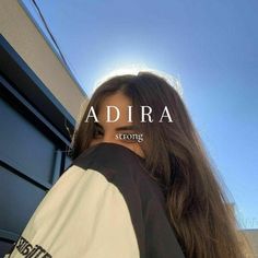 a woman with long brown hair standing in front of a blue building and the words adria strong above her head