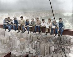 a group of men sitting on top of a tall building in the middle of a city