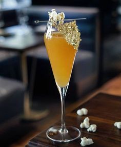 a glass filled with liquid sitting on top of a wooden table next to white popcorn