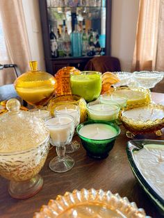 a wooden table topped with lots of dishes and glasses filled with liquid next to candles