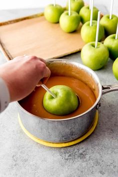 a person stirring apples in a pot with sticks sticking out of the top and green apples behind them