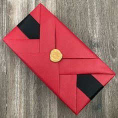 an origami envelope with a gold button on it sitting on a wooden surface