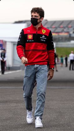 a man wearing a face mask while walking across a race track with his hands in his pockets