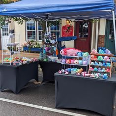 two tables with stuffed animals on them under a blue tarp in front of a store