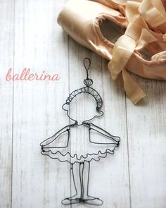 a wire ballerina ornament sitting on top of a wooden floor next to a ballet shoe