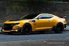 a yellow sports car parked on the side of the road next to a brick wall