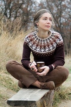 a woman sitting on top of a wooden bench holding a coffee cup in her hands